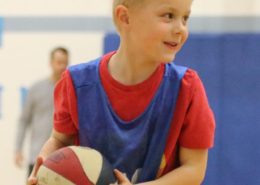 Boy holding a basketball. He has a huge smile and a glint in his eye.