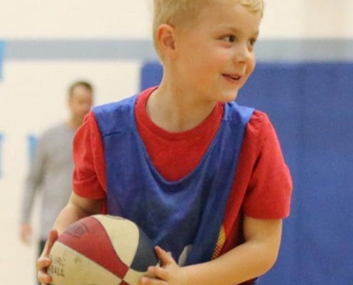 Boy holding a basketball. He has a huge smile and a glint in his eye.