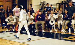 A fencer returns after scoring a point. His teammates cheer wildly behind him.